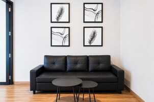Una sala de estar moderna con un sofá de cuero negro, dos mesas redondas negras y cuatro cuadros abstractos enmarcados en la pared.