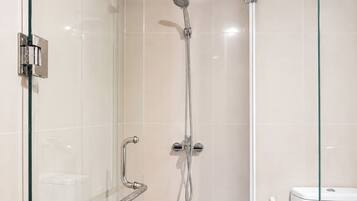 A glass-enclosed shower with a handheld showerhead and a wall-mounted faucet.