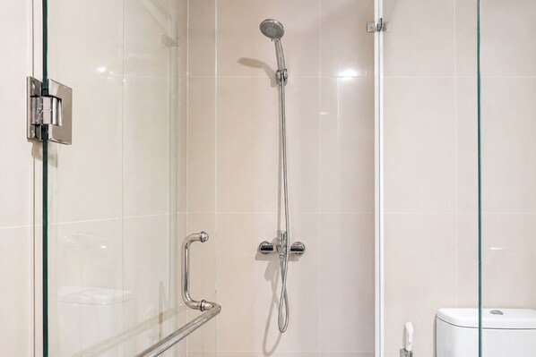 Ducha con cerramiento de vidrio, cabezal de ducha manual y llave de pared.