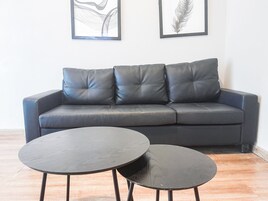 A dark grey sofa with four cushions, two framed artworks on the wall, and two round black tables with metal legs.