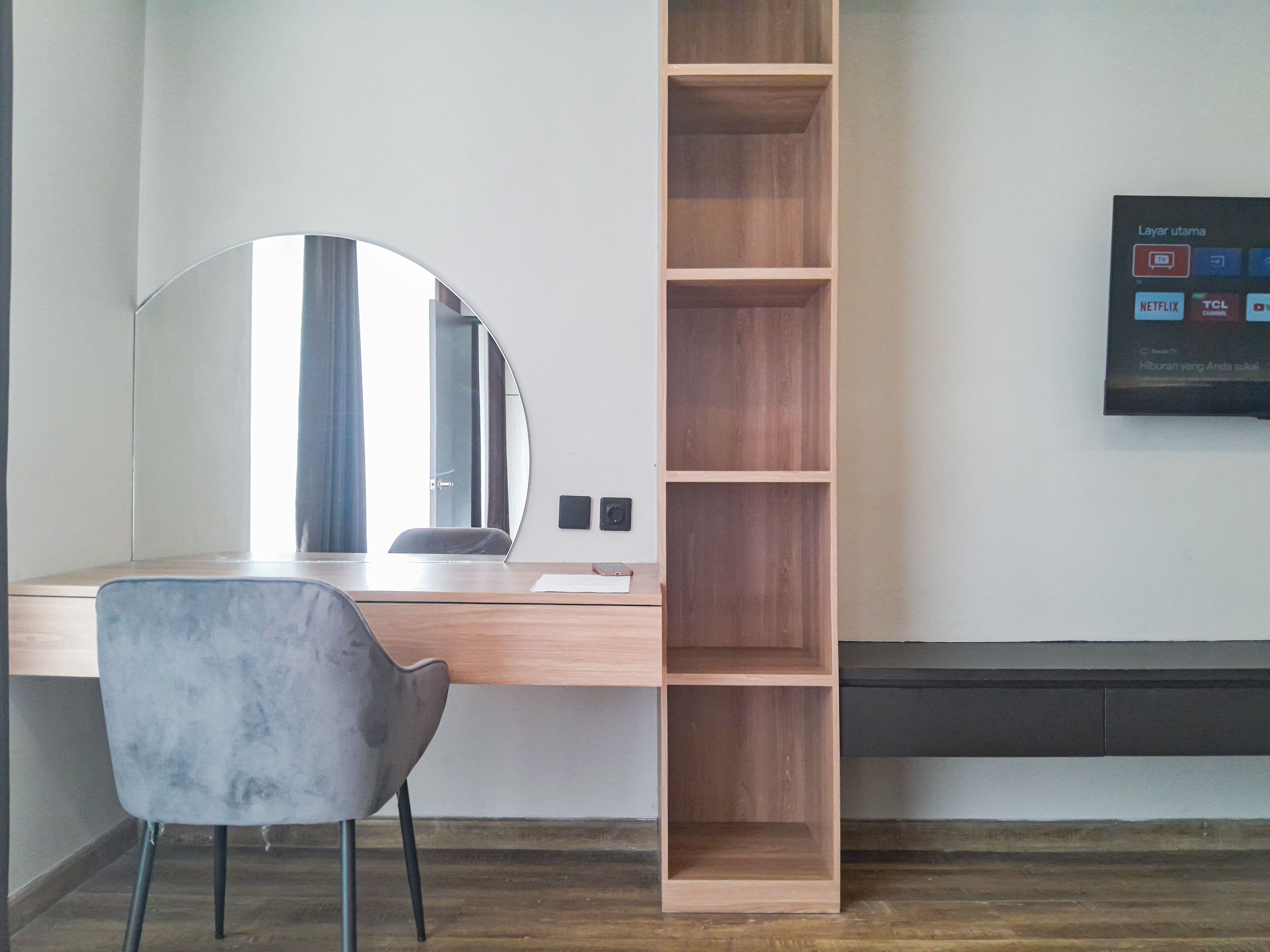 A modern office desk with a chair, a large mirror, and a wooden shelving unit.