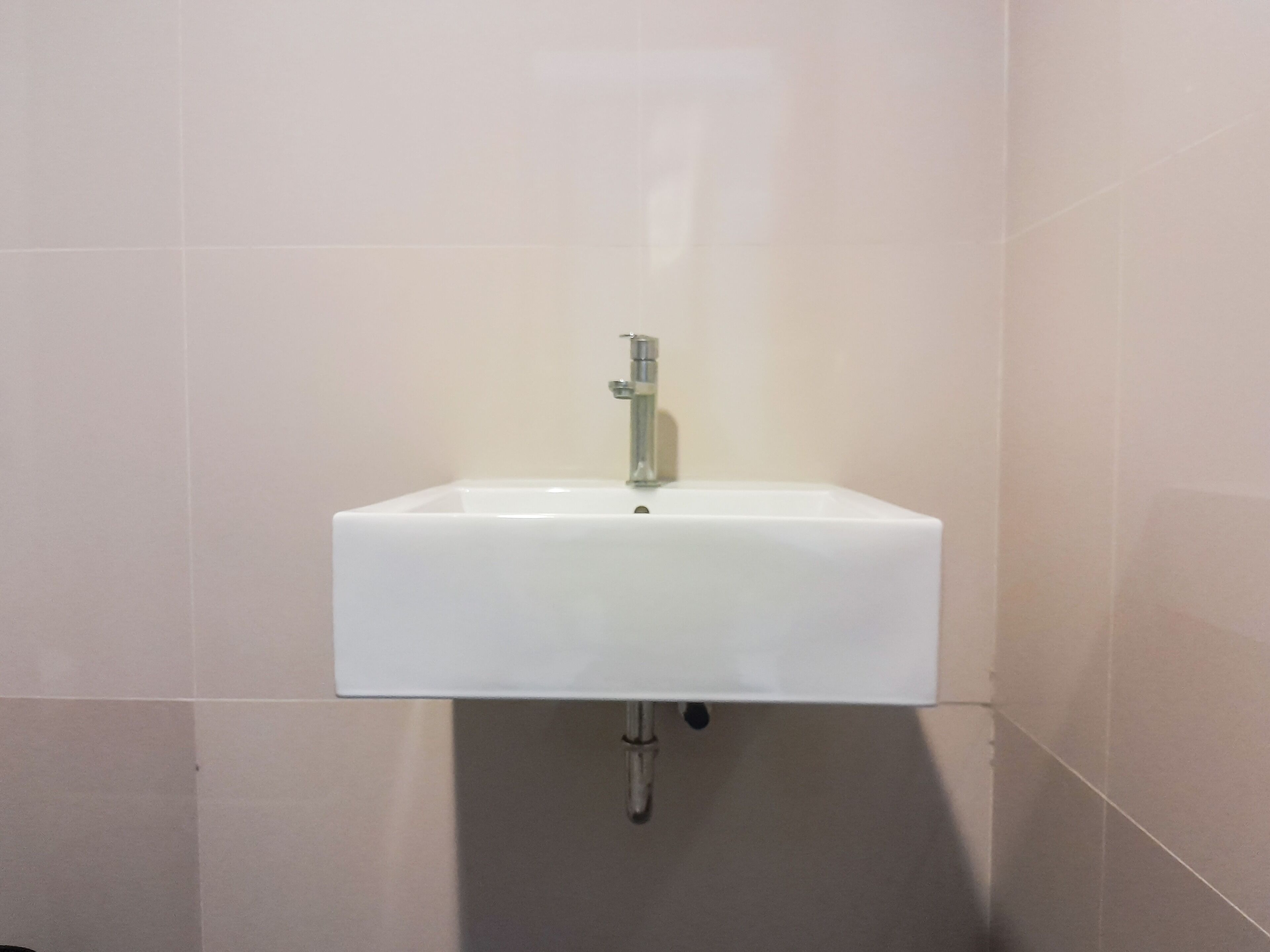 A white bathroom sink with a chrome faucet mounted on a tiled wall.