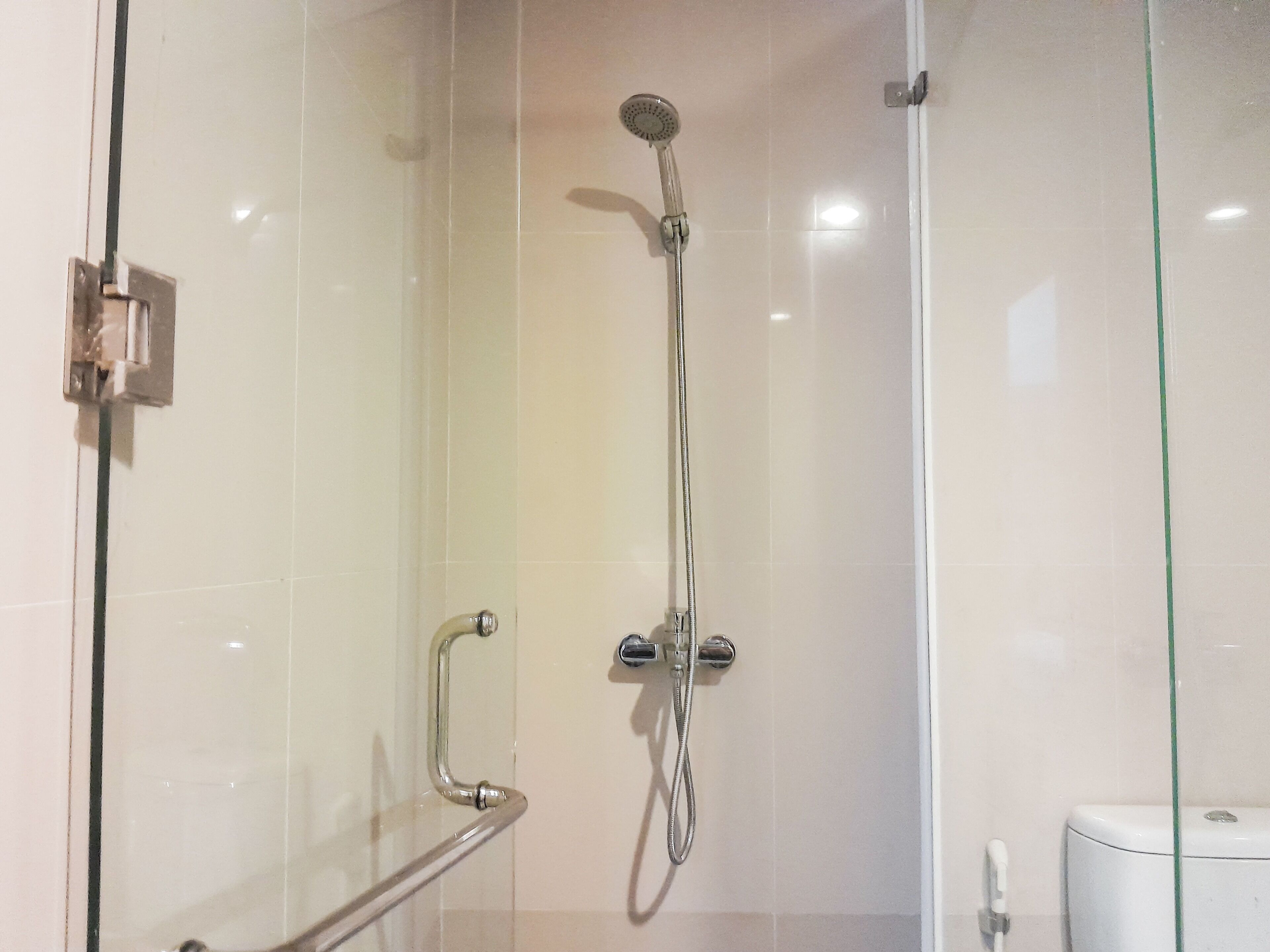 A glass-enclosed shower stall with a handheld showerhead and a handheld faucet.