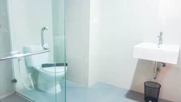 Une salle de bain avec une douche à parois de verre, un lavabo blanc et une poubelle.