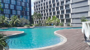 Una piscina con muelle de madera, rodeada de palmeras y edificios modernos.