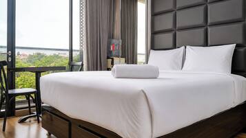Quarto de hotel com uma cama grande, uma escrivaninha e vista para o verde.
