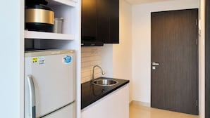 A compact kitchen with a refrigerator, a sink, and a dark wooden door. - Cozy And Chic Studio At Apartment Tamansari Skylounge Balikpapan (Balikpapan)