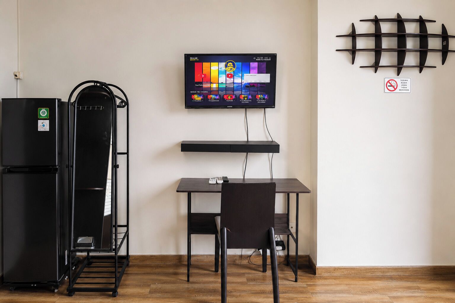 Une petite cuisine équipée d’un réfrigérateur, d’un four à micro-ondes et d’un téléviseur à écran plat fixé au mur.