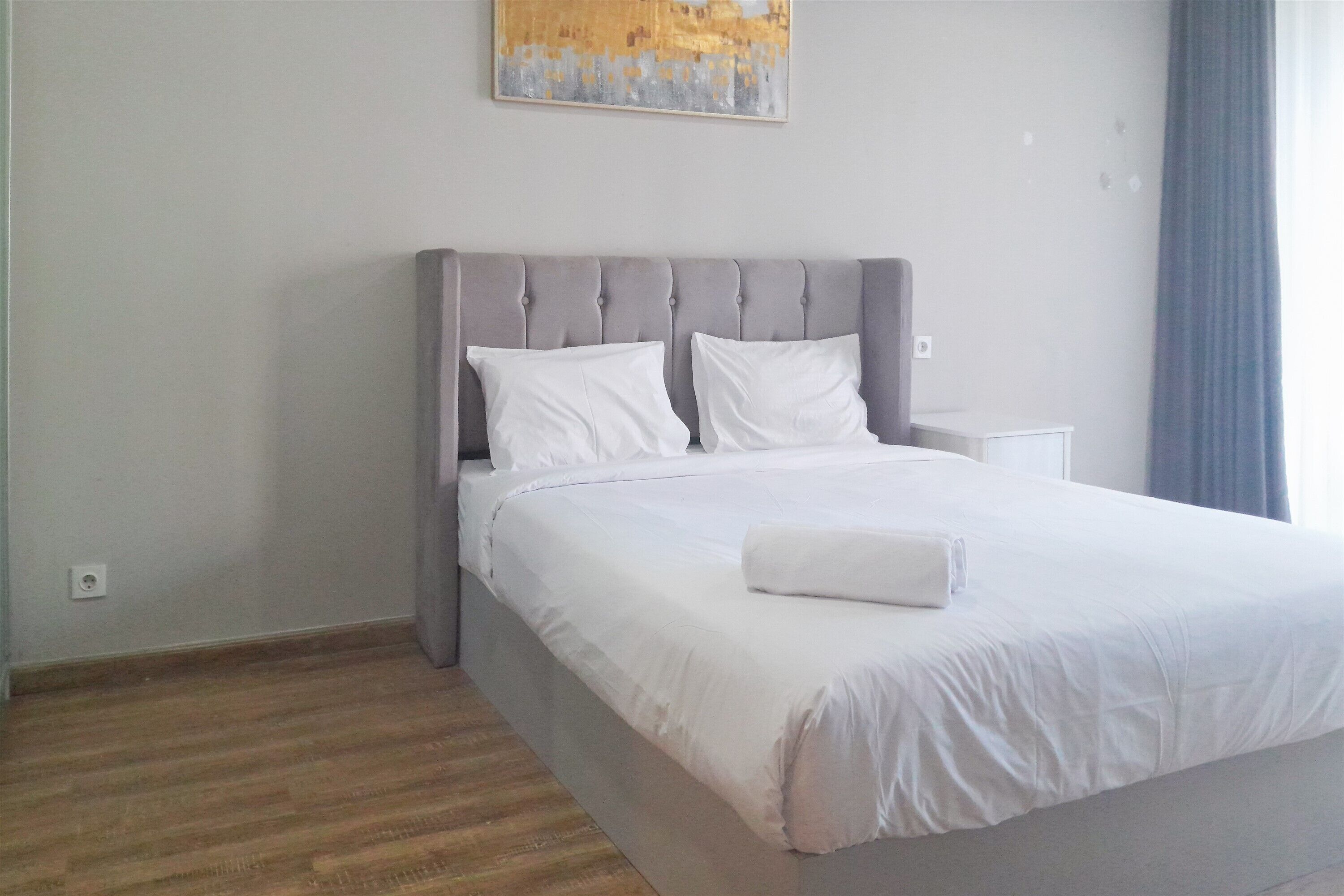 Un lit bien fait, avec du linge de lit blanc, une tête de lit rembourrée de couleur grise et un oreiller blanc.