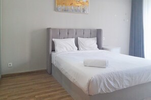 Una cama bien hecha con sábanas blancas, un cabecero tapizado en gris y una almohada blanca.
