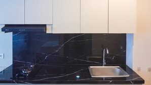A kitchen with a black marble countertop, stainless steel sink, and a black range hood. - Functional Nice Studio Room At Apartment Tamansari Skylounge Balikpapan (Balikpapan)
