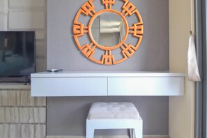 A room with a white console table, a round mirror with an orange frame, and a small white bench. - Warm Living In Studio Room At Apartment Tamansari Skylounge Balikpapan (Balikpapan)