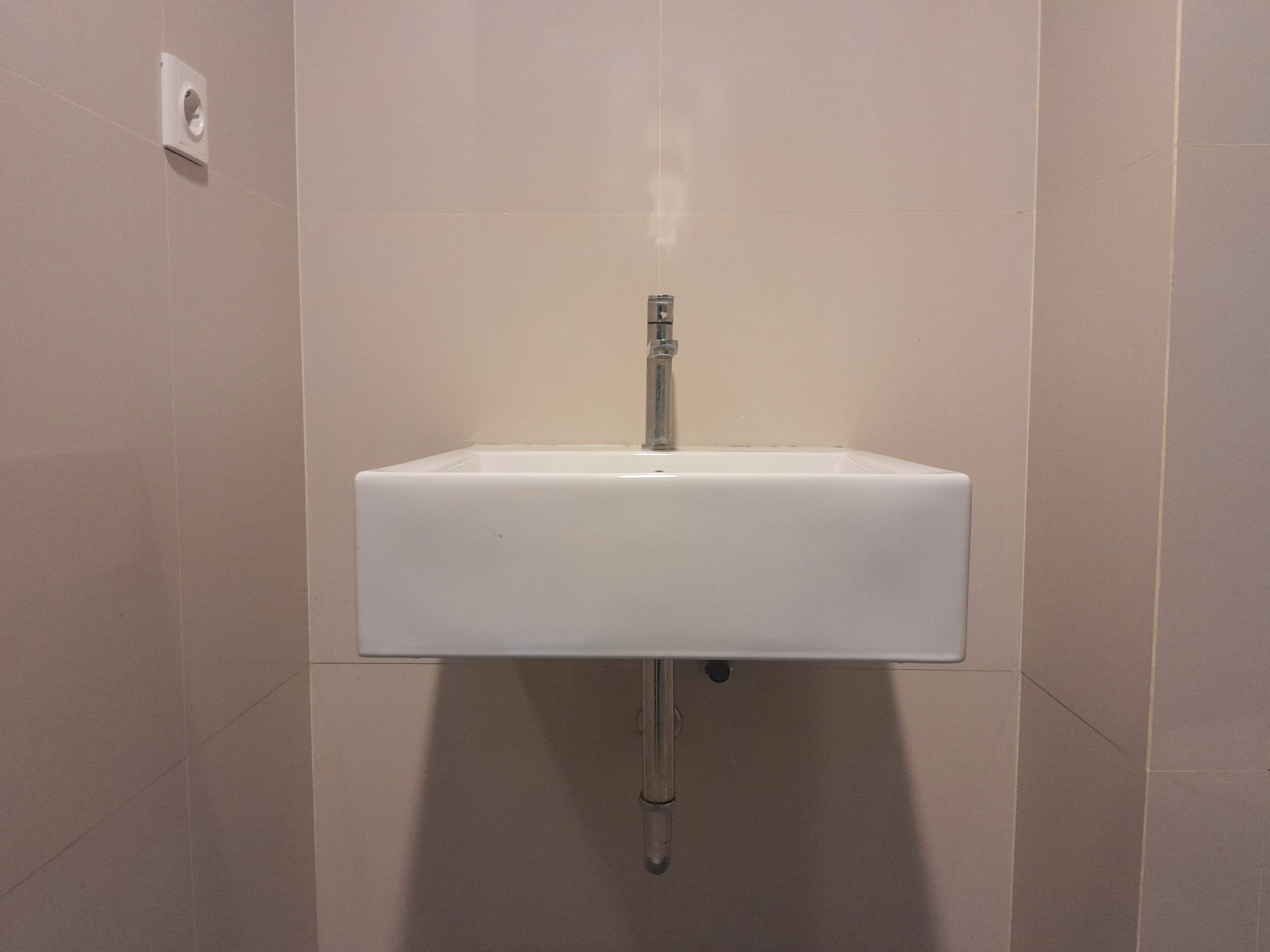 A white bathroom sink with a chrome faucet, mounted on a wall with a single light switch above it.