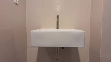 Ein weißes Waschbecken mit chromfarbenem Wasserhahn, an der Wand montiert, darüber ein Lichtschalter.
