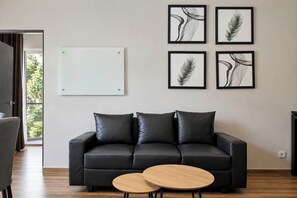 Ein modernes Wohnzimmer mit einem schwarzen Ledersofa, zwei runden Couchtischen aus Holz und vier gerahmten abstrakten Kunstwerken an der Wand.