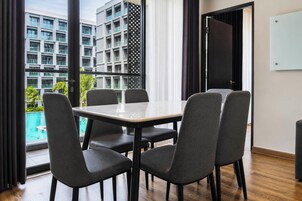 Un salón de conferencias con una mesa de vidrio y cuatro sillas, ventanas amplias con vista a un edificio y una piscina, y una puerta con marco negro.