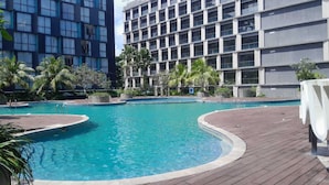 En swimmingpool med træterrasse, omgivet af palmer og moderne bygninger.
