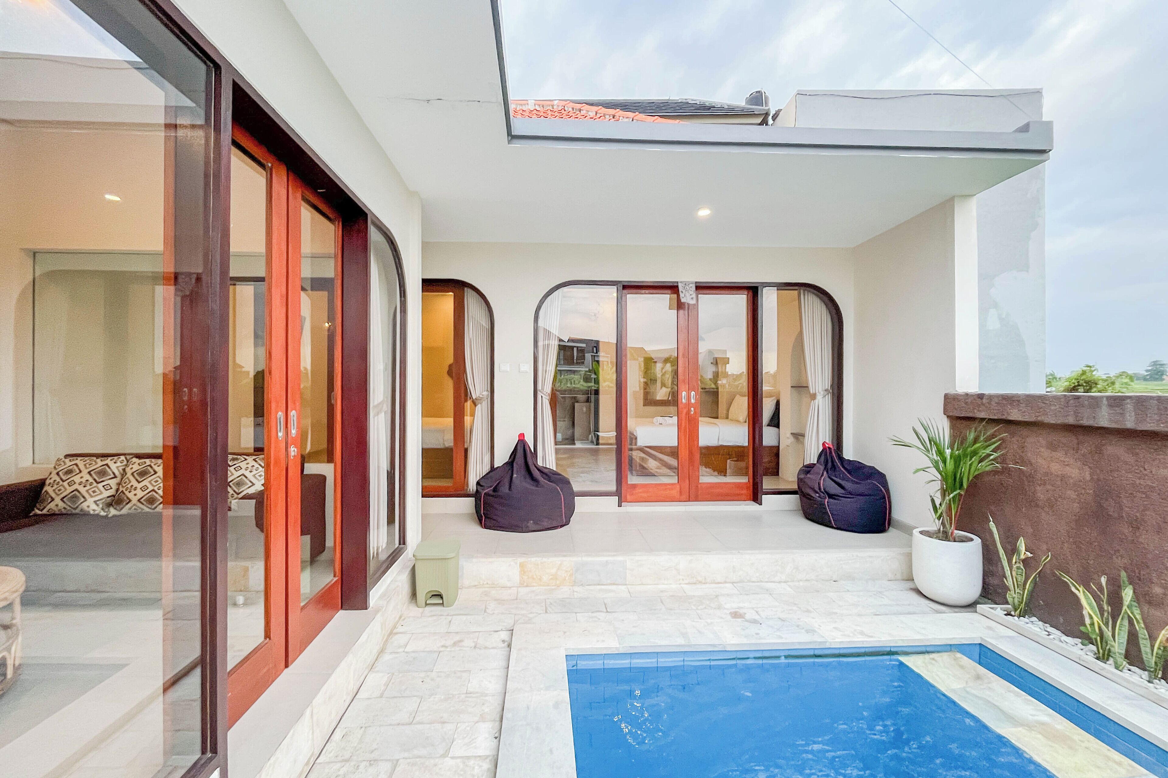 A modern outdoor pool area with a glass door entrance, a small seating area with cushions, and a potted plant.