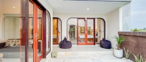 A modern outdoor pool area with a glass door entrance, a small seating area with cushions, and a potted plant.
