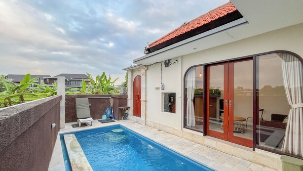 A swimming pool with a tiled deck, a covered patio with a table and chairs, and a view of neighboring buildings. - 2BR Damar Pererenan Villa Near Canggu (Bali)