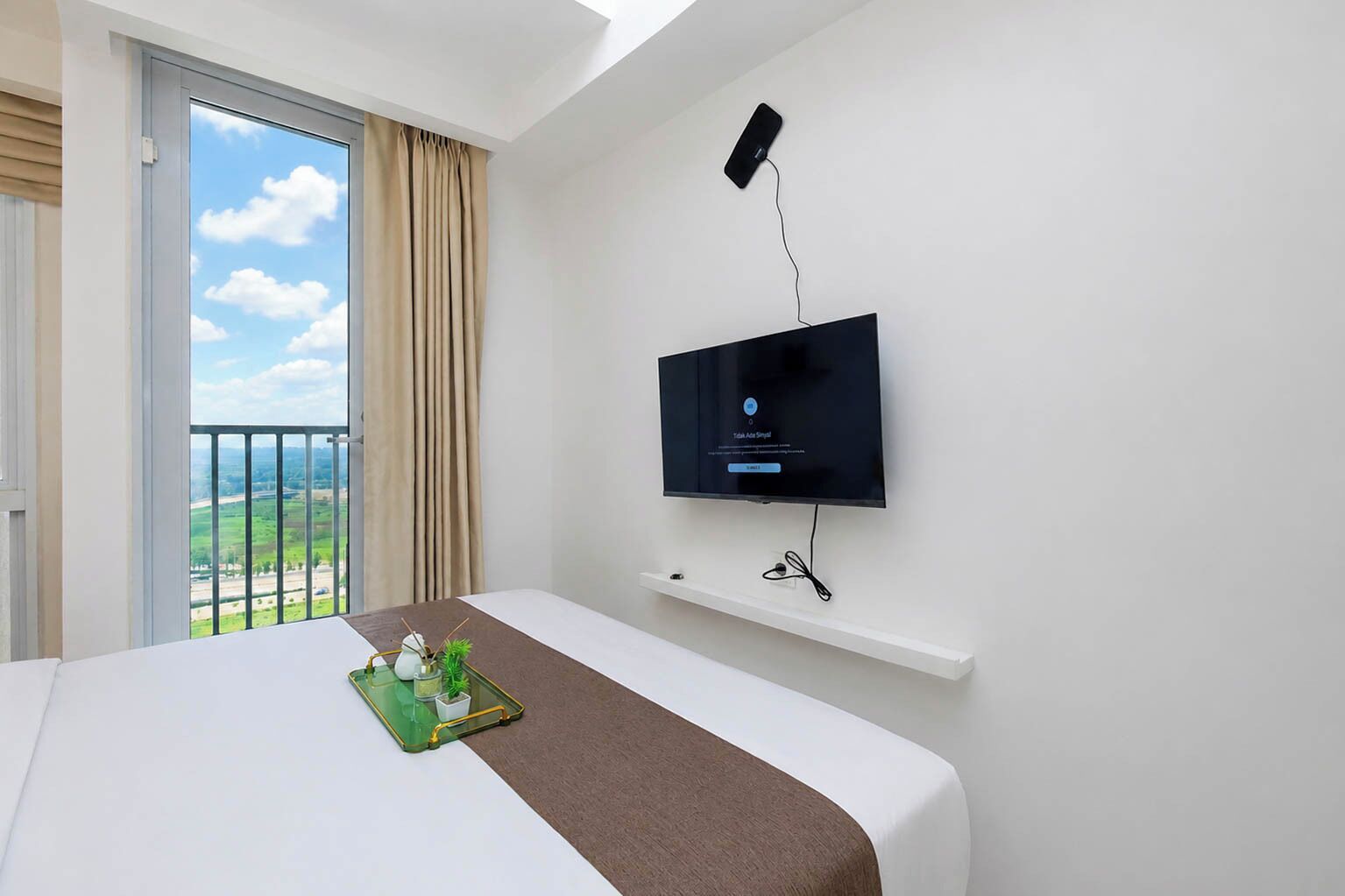 Ett hotellrum med en säng, en tv som är monterad på väggen, en balkong med utsikt och en liten hylla under tv:n.