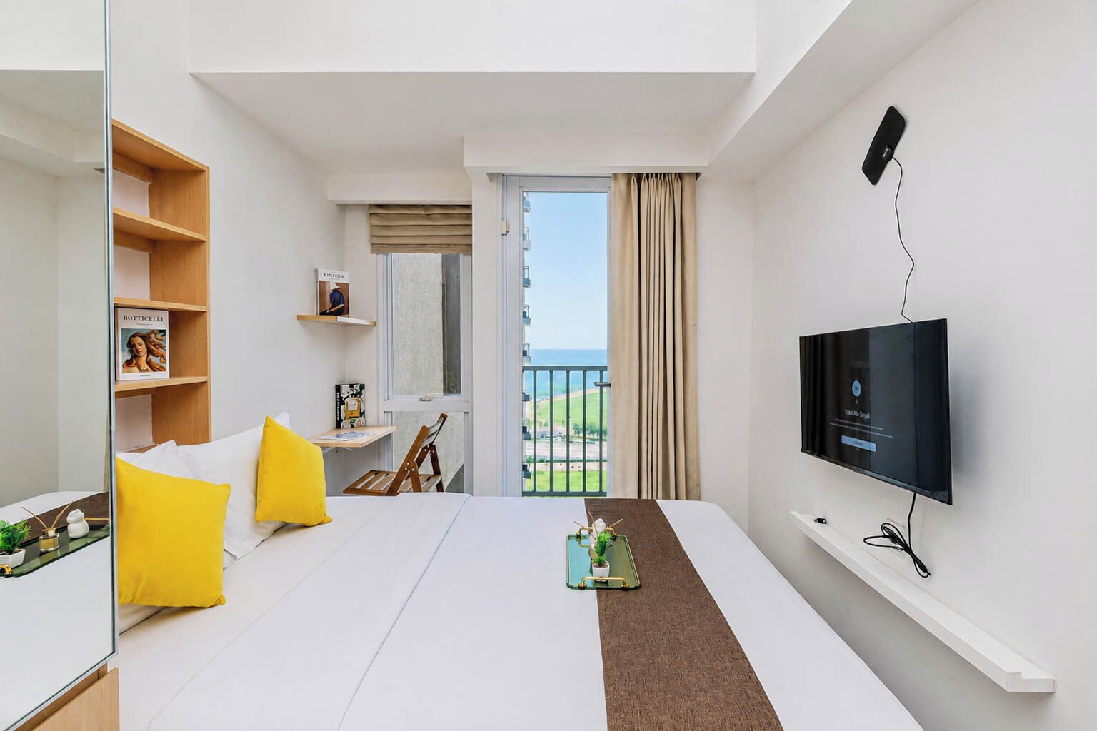 A hotel room with a bed, a TV, a balcony with a view, and a small table with a plant.