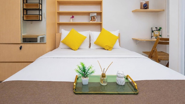 Une chambre d’hôtel bien rangée, avec un lit, un petit bureau et une étagère contenant des livres et un tableau.