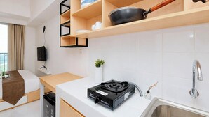 Une cuisine de taille réduite, équipée d’une cuisinière à gaz, d’un évier et d’étagères en bois au-dessus.