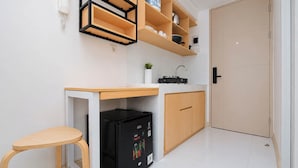 Une cuisine compacte dotée d’un réfrigérateur encastré, de meubles de rangement en bois, d’un plan de travail et d’un tabouret.