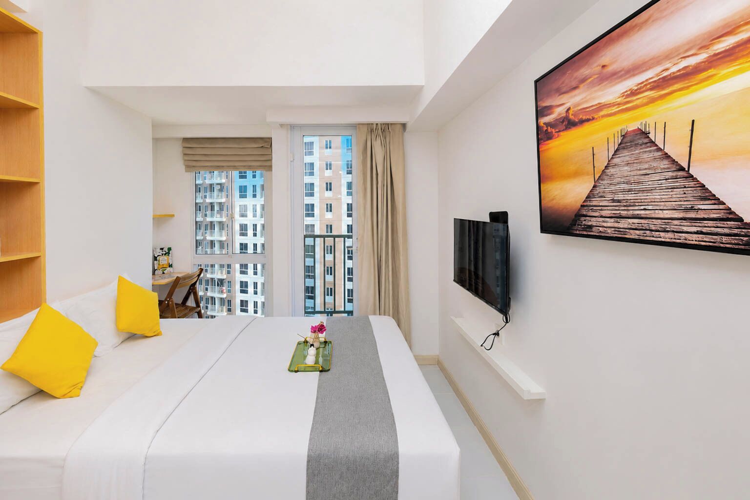 A hotel room with a bed, a desk, a TV, and a view of the cityscape.