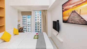 A hotel room with a bed, a desk, a TV, and a view of the cityscape.