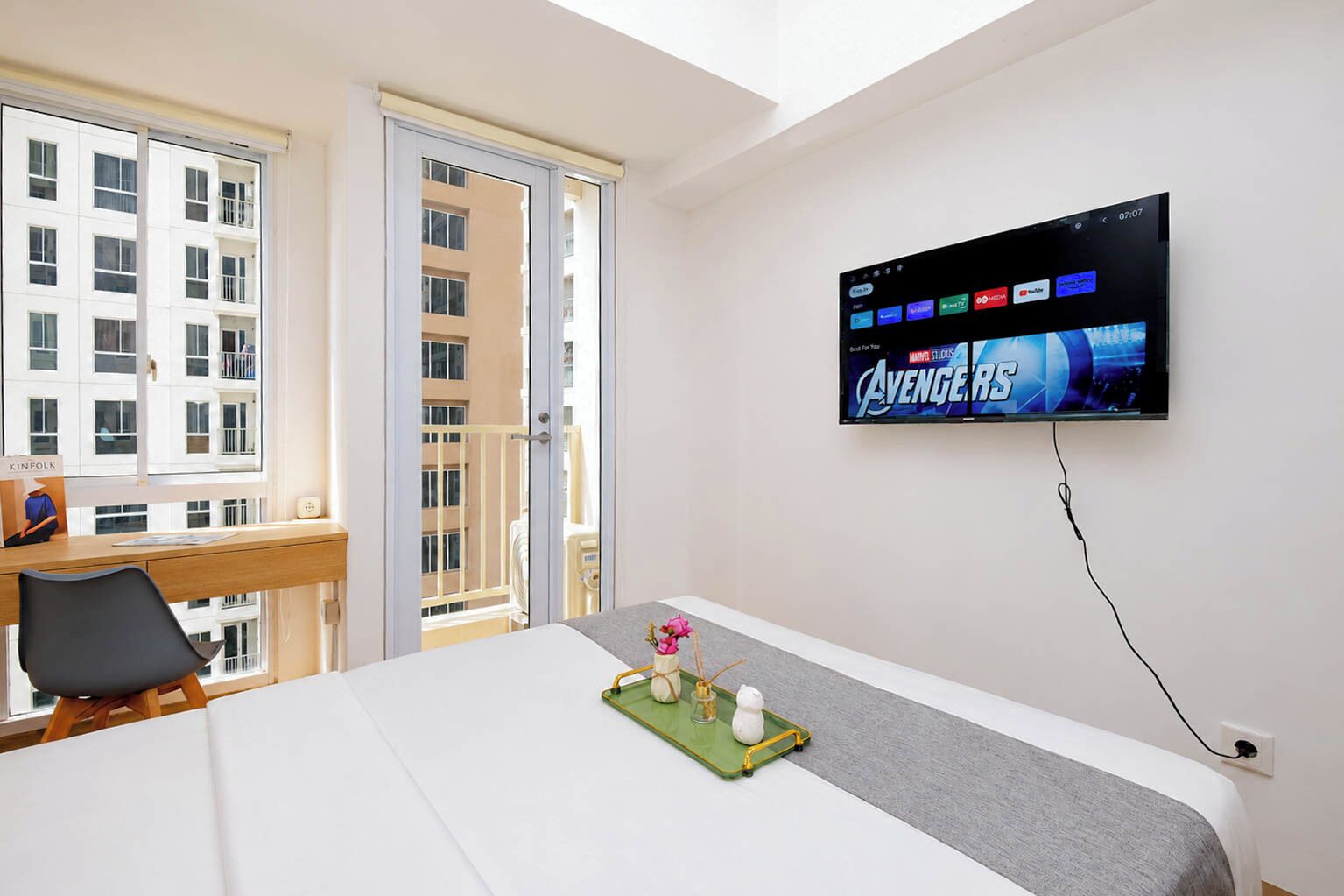 Hotellihuone, jossa on sänky, työpöytä, tuoli, seinälle asennettu televisio ja parveke, jolta on näkymä muihin rakennuksiin.