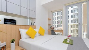 Une chambre d’hôtel moderne équipée d’un lit, d’un bureau, d’une chaise, d’une petite table avec un vase et d’une fenêtre donnant sur d’autres immeubles.