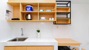 A modern kitchen with a sink, countertop, wooden cabinets, a kettle, a rice cooker, and a small potted plant. - Clean And Warm Studio Room At Apartment Tokyo Riverside Pik 2 (Teluknaga)