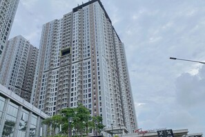 A high-rise residential building with multiple balconies, a modern glass facade, and a sign indicating a nearby university. - Clean And Warm Studio Room At Apartment Tokyo Riverside Pik 2 (Teluknaga)