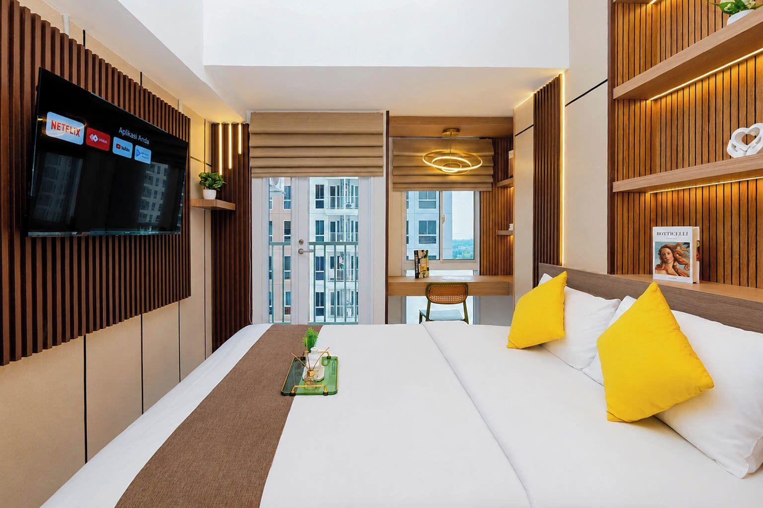 Quarto de hotel com cama, televisão na parede, escrivaninha e vista para a cidade.