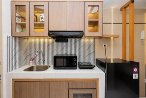 A compact kitchen with a microwave, toaster, and a black refrigerator. - Warm And Homey Studio At Apartment Tokyo Riverside Pik 2 (Jakarta)