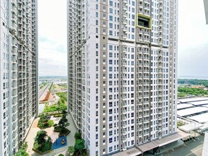 A high-rise residential building with multiple balconies, a central courtyard with greenery, and a view of the surrounding area. - Good Deal And Minimalist Studio Apartment At Tokyo Riverside Pik 2 (Jakarta)