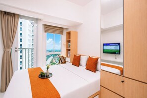 A hotel room with a bed, a TV, a window with a view, and a balcony. - Good Deal And Minimalist Studio Apartment At Tokyo Riverside Pik 2 (Jakarta)