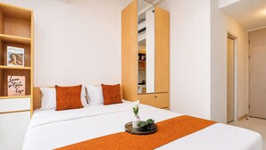 A modern hotel room with a large bed, a bedside table, a wardrobe, and a shelf with decorative items. - Good Deal And Minimalist Studio Apartment At Tokyo Riverside Pik 2 (Jakarta)