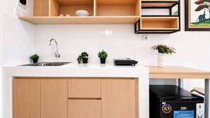 A kitchen with a white countertop, wooden cabinets, a stainless steel sink, and a black refrigerator. - Good Deal And Minimalist Studio Apartment At Tokyo Riverside Pik 2 (Jakarta)