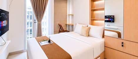 A modern hotel room with a large bed, a TV, a wooden wardrobe, and a window with curtains.