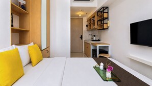 Ein Hotelzimmer mit einem Bett, einer kleinen Küchenzeile, einem an der Wand montierten Fernseher und einem Regal mit Büchern.