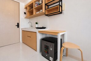 A compact kitchen with a built-in refrigerator, a wooden countertop, and a single chair. - Good Deal And Homey Studio Apartment Tokyo Riverside Pik 2 (Jakarta)