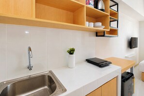 A modern kitchen with a stainless steel sink, wooden cabinets, a white countertop, and a small potted plant. - Good Deal And Homey Studio Apartment Tokyo Riverside Pik 2 (Jakarta)