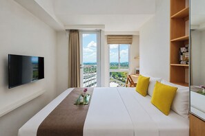 A hotel room with a bed, a TV, a window with a view, and a bookshelf. - Good Deal And Homey Studio Apartment Tokyo Riverside Pik 2 (Jakarta)