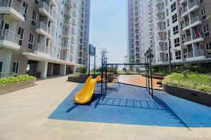 Un parque infantil con un tobogán amarillo y una estructura para escalar en una zona residencial con edificios altos.