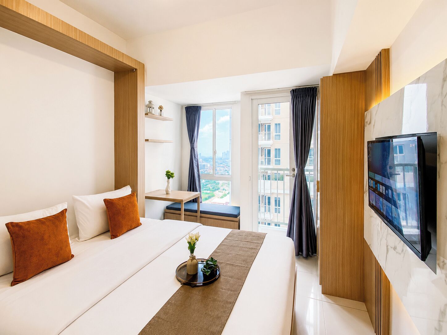 Une chambre d’hôtel avec un lit, une télévision, une petite table avec une plante et une vue sur les bâtiments par la fenêtre.