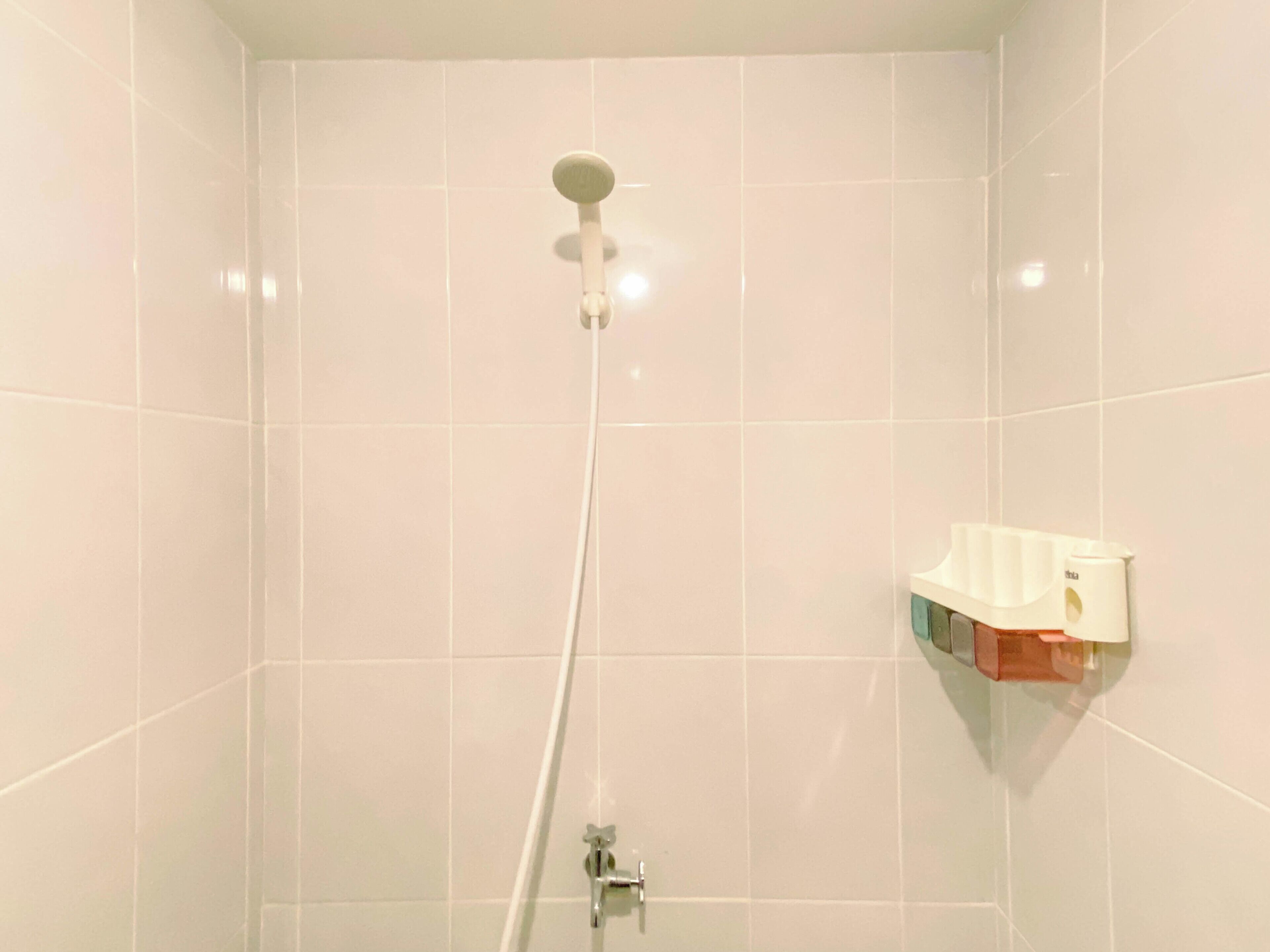 Chuveiro com chuveiro manual, torneira fixa na parede e dispensador de sabonete.