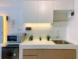 A modern kitchen with white cabinets, a stainless steel sink, a microwave, and a small refrigerator.